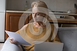 Serious senior homeowner lady doing domestic paperwork at home