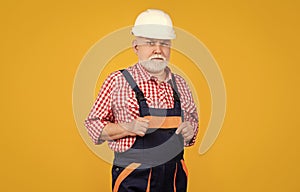 serious senior man builder in helmet on yellow background
