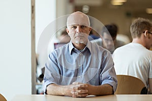 Serious senior man sitting alone in crowded place