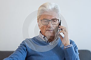 Serious senior man talking on phone in living room