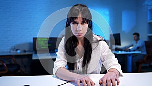 Serious slim beautiful woman putting on headphones and typing on keyboard. Portrait of concentrated Caucasian hacker