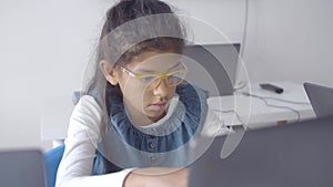 Serious smart schoolgirl in glasses sitting at desk