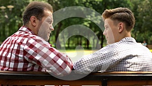 Serious son and dad talking on bench in park, father sharing life experience