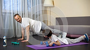 Serious sportive family doing plank exercise with dumbbells at home, role model
