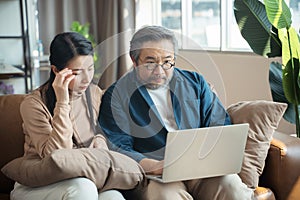 Serious stressed Middle-aged Asian couple finances calculate bills tax on the laptop.