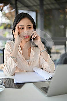 Serious and stressed millennial Asian businesswoman is on the phone with someone