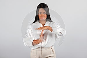 Serious strict confident millennial black businesswoman in white blouse make time out sign with hands