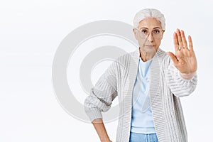 Serious and strict old woman, grandmother forbid, stretch arm forward in stop, rejection or prohibition gesture, look photo