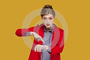 Serious strict woman with red lips standing pointing finger to her smartwatch, looking at camera.