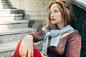 Serious student female looking away, sitting on the stairs next to the college campus on a sunny day. A pretty sad woman in a