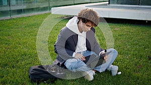 Serious student typing laptop at urban park. Relaxed youngster sitting grass