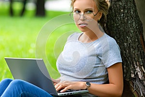 Serious student woman in eyeglases in city park with laptop.