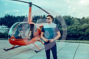 Serious stylish dark-haired man in sunglasses and dark shirt waiting for pilot
