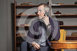 Serious successful businessman in blue suit talking on mobile phone and holding his eye glasses in his hand