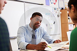 Serious teacher at desk talking to adult education students photo
