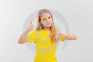 Serious teen girl, frowns and points thumbs up and down with disappointed face expression, stands in casual yellow t shirt over