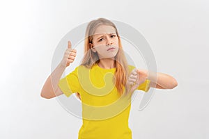 Serious teen girl, frowns and points thumbs up and down with disappointed face expression, stands in casual yellow t shirt over