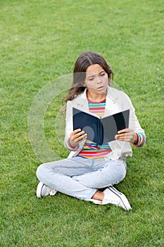 serious teen girl read book sitting on grass. reading book. reader girl with book outdoor