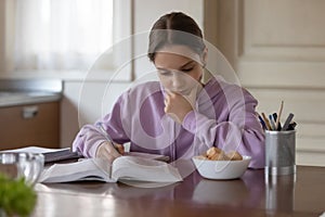 Serious teen girl school pupil studying at home kitchen table