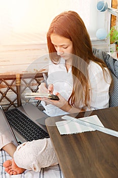 Serious teenage girl sits in her pajamas and learns remotely via the Internet during quarantine. Writes with a pen in a