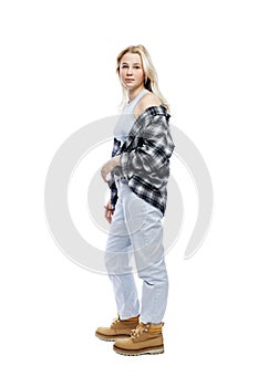 Serious teenage girl standing. Cute blonde girl in jeans, plaid shirt and yellow shoes. Full height. Isolated on a white