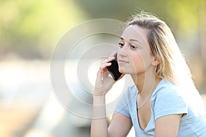 Serious teenage girl talking on phone in a park