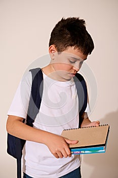 Serious teenage schoolboy in white mockup t-shirt and blue jeans, holding copybooks, isolated on white studio background