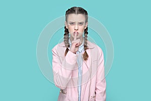 Serious teenager girl keeps finger near lips, showing shh gesture, asking to keep silence.