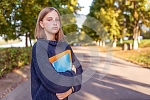 Serious teenager girl with smart look, stands summer park, background autumn trees, free space copy text. In hands
