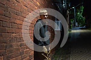 Serious teenager leaning against a brick wall.