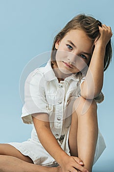 Serious little girl in a white thick romper suit sitting on the floor photo