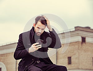 Serious thinking business man in fashion clothing texting sms looking on mobile phone in the hand outdoors autumn background