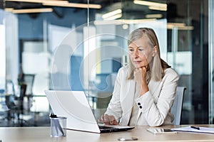 Serious thinking businesswoman working inside office with notebook, mature senior woman boss with gray hair at workplace