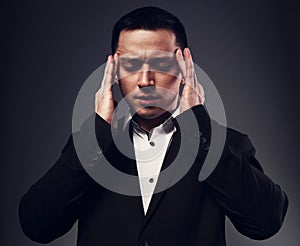 Serious thinking man with thought-transference abilities holding the hands the head with closed eyes in black suit on grey studio