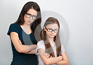 Serious thinking mother and sad doubt kid in glasses with folded arms on light blue background. Closeup studio portrait. Online