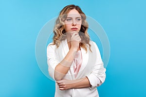 Serious thinking. Portrait of pensive woman touching her chin and considering idea, deep in thoughts. blue background