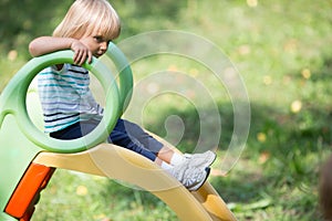 Serious thinking or sad young baby caucasian blonde girl on slide outdoor
