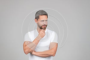 Serious thoughtful man in white tshirt stroke chin thinking grey background, think