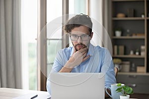 Serious thoughtful millennial man staring at laptop, read received message