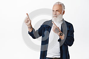Serious thoughtful old man with tattoos, pointing and looking upper left corner, thinking to buy, making choice in store