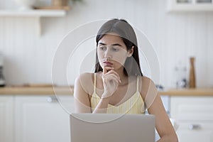 Serious thoughtful student girl sitting at laptop at home