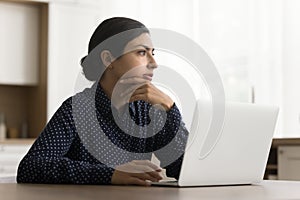 Serious thoughtful student girl sitting at laptop at home