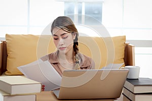 Serious tired beautiful woman reads many document papers, analyzes data information, uses laptop computer. Thoughtful confused