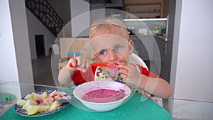 Serious toddler child eating beetroot soup sitting near table. Gimbal motion