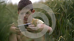 Serious tortured boy is playing in the phone on the wheat field