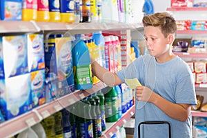 Serious tweenager boy looking household chemicals with shopping list