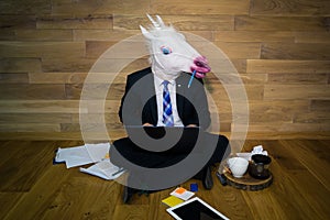 Serious unicorn in a suit and tie enthusiastically works at home with cup of coffee on wooden stand