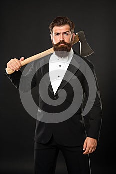 Serious unshaven man with beard and moustache in formal suit holding axe dark background, brutal