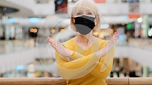 Serious upset mature woman in medical mask stands in public place looking at camera arms crossed in front makes
