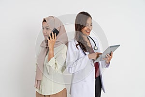 serious veiled woman making a call with mobile phone and beautiful female doctor using tablet with back to back pose